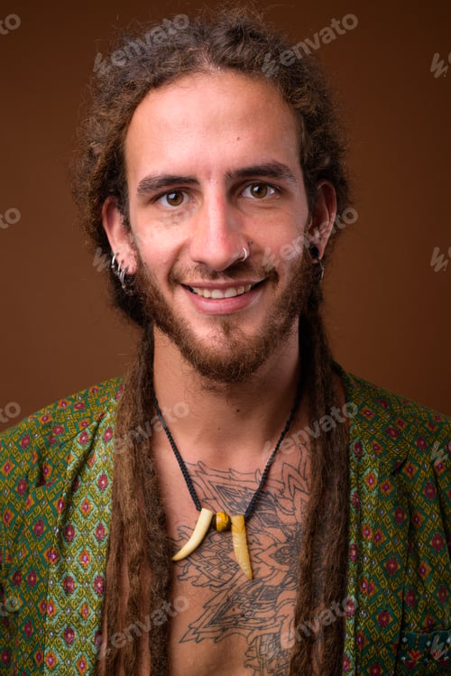 Preview: Young handsome Hispanic man with dreadlocks against brown backgr