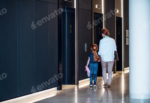 Preview: A rear view of businesswoman with small daughter walking in office building