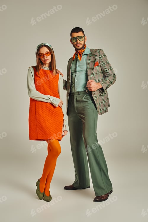 Preview: young couple in stylish vintage attire and sunglasses standing on grey backdrop, full length