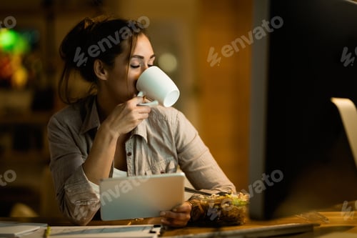 Preview: Young woman drinking tea with eyes closed while using digital tablet at night.