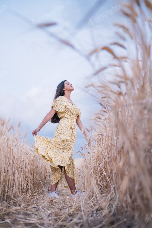 Preview: Young brunette woman enjoying the nature while standing in the middle of a wheat field.