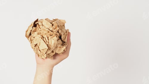 Preview: The man's hand is holding crumpled brown paper ball on white background.