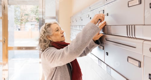 Preview: Senior woman opening communal mailbox checking for mail