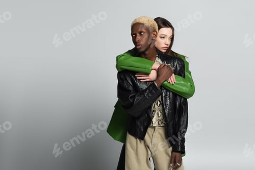 Preview: young woman hugging blonde african american man in black leather jacket on grey