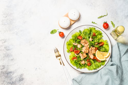 Preview: Green salad with baked fish at white table.