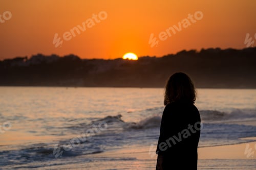 Preview: Of a woman standing on a sandy beach during a beautiful sunset