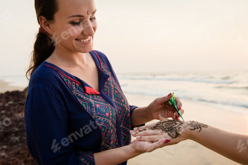 Preview: Smiling artist applying henna tattoo on women hands outdoors. Mehndi is traditional Indian decorativ