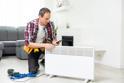 Preview: Man in work overalls using wrench while installing heating radiator in room. Young plumber