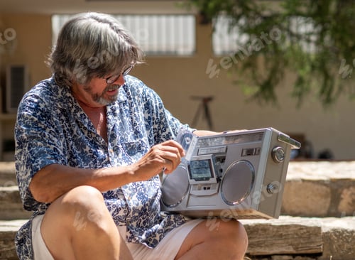 Preview: Mature man with grey hair and beard, tries to set in motion an old radio cassette