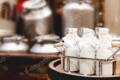 Preview: Glass bottles with fresh natural milk, aluminum cans on hay on dairy farm. Healthy farm products.