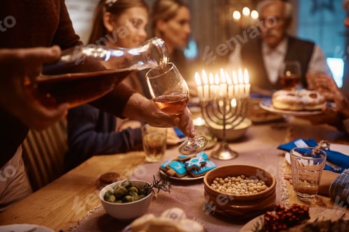 Preview: Close up of Jewish man pouring wine into wineglass while celebrating Hanukkah with his family .
