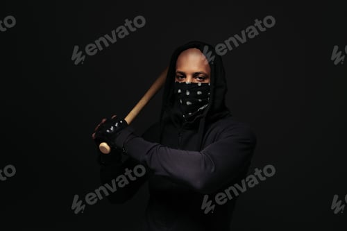 Preview: African american hooligan with mask on face holding baseball bat isolated on black