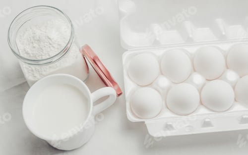 Preview: Eggs, a cup of milk and flour on white background