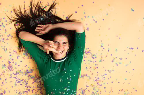 Preview: Young woman lying down on confetti covered floor, having fun