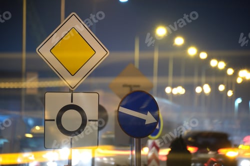 Preview: Roundabout road signs with blurred cars on city street traffic at night. Urban transportation