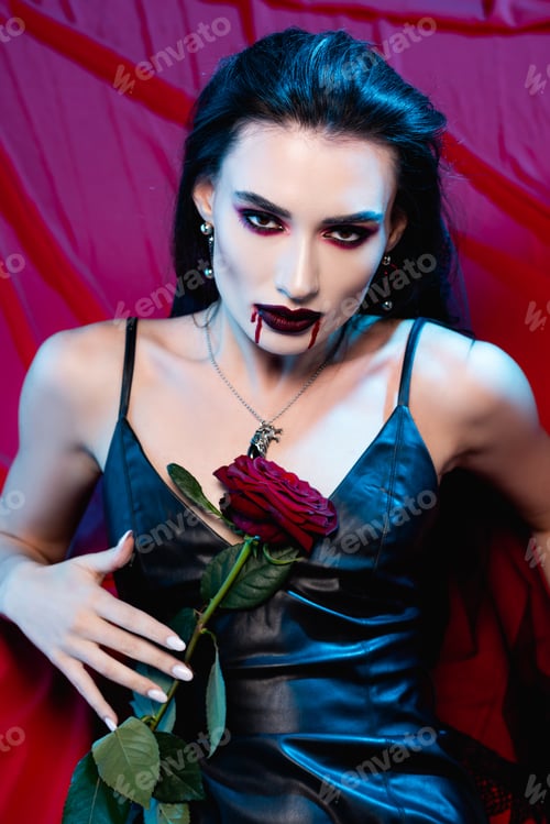 Preview: pale woman with blood on face looking at camera and holding rose on red