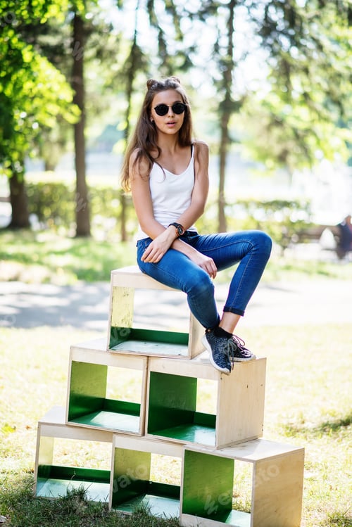 Preview: Portrait of a fashionably dressed girl posing on wooden boxes in the park on a sunny day
