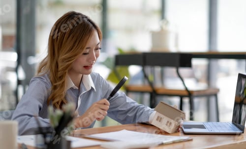 Preview: Close up of businesswomen holding magnifying glass finding a wooden shape of a house, realtor, agent