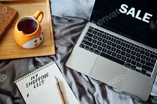 Preview: Black Friday sale. Shopping List in note book near laptop with word Sale and tea coffee cup at bad