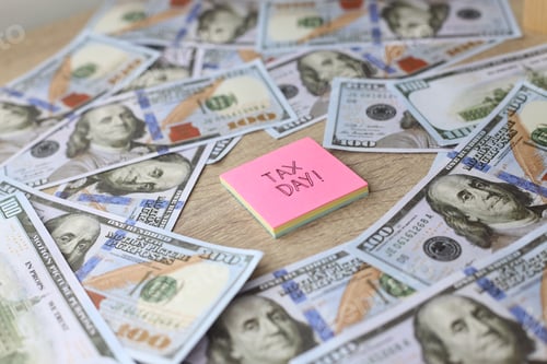 Preview: Tax day written on a sticky note against the dollar bills
