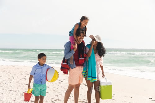 Preview: Happy biracial man carrying daughter on shoulders while walking with woman and son at beach