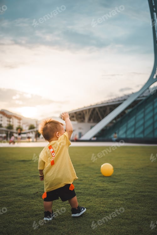Preview: Little boy playing football in a garden during sunset