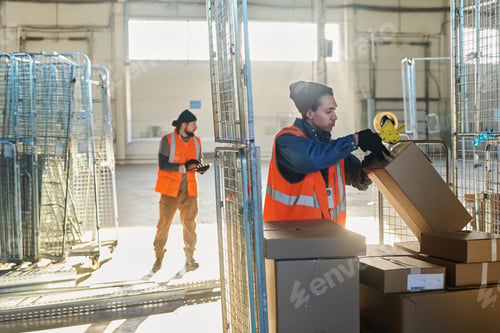 Preview: Young man in protective workwear standing by stack of boxes
