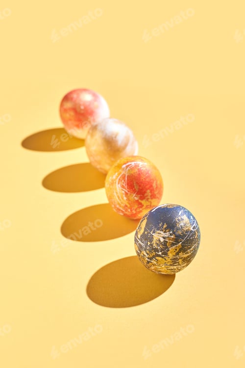 Preview: Colorful marbled balls in warm tones on yellow background casting shadows