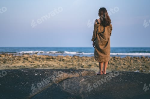 Preview: Rear view of a beautiful asian woman standing alone on the beach by the seashore