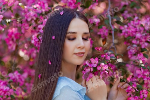 Preview: A girl with pink petals in long hair is standing near a blooming
