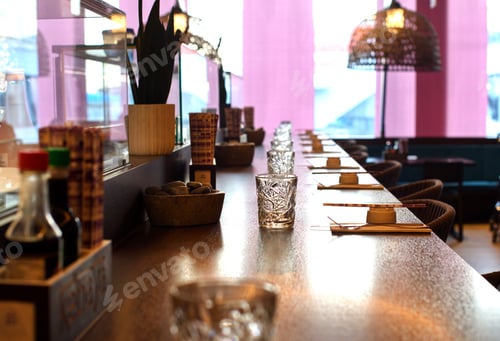 Preview: Empty sushi bar place settings with chopsticks and glass. Pink background with sun blur windows