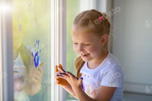 Preview: Portrait of a happy little girl draw palms on the window.