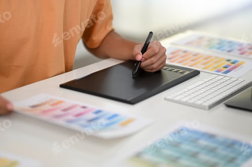 Preview: Hand with pen writing on digital board with color chart on designer desk.