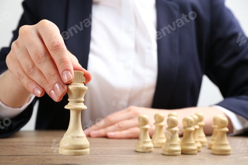 Preview: Woman with chess piece at wooden table, closeup. Career promotion concept