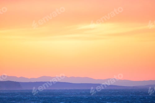 Preview: Scenic view of a stunning sunset over the ocean, with colorful mountains in the background