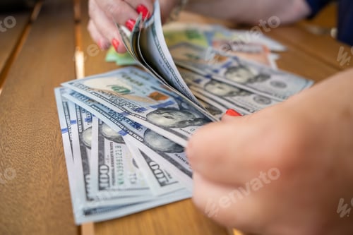 Preview: Closeup of female hands counting dollar bills on a wooden surface