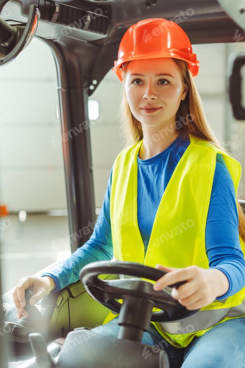 Preview: Beautiful woman, operator, driver wearing hard hat, workwear driving forklift, working in warehouse