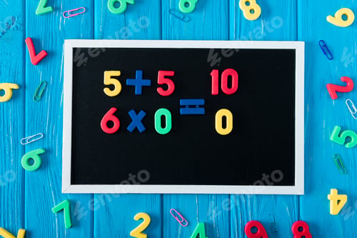 Preview: top view of blackboard with math sums, colorful numbers and paper clips on blue wooden background