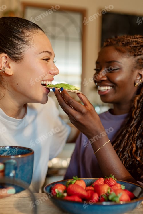 Preview: Happy lesbian couple sharing avocado toast at breakfast table
