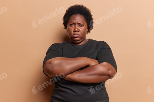 Preview: Photo of offended dark skinned curly haired woman with excess weight keeps arms folded has sulking