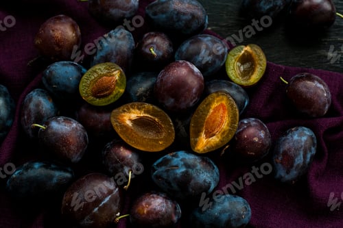 Preview: Dark ripe juicy plums lie on a purple tablecloth