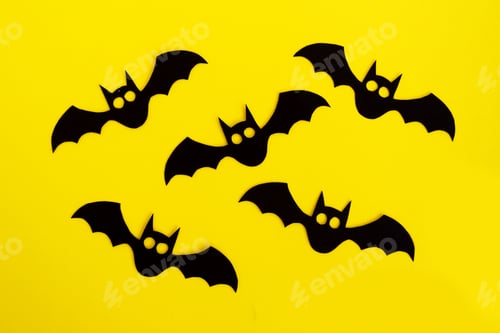 Preview: Holiday decorations for Halloween. Five black paper bats on a yellow background, top view.