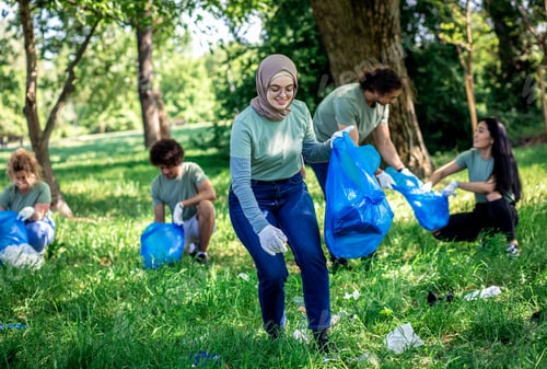 Preview: Portrait of young Muslim woman with garbage bag cleaning city park with friends.