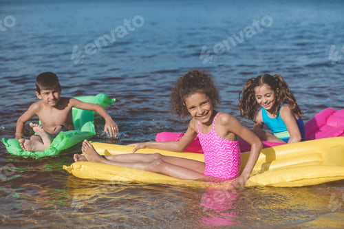 Preview: multiethnic little children swimming on colorful inflatable mattresses at sea together