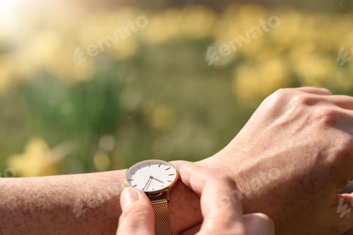 Preview: Woman is checking the time on her wristwatch with blurry yellow spring flowers in the background