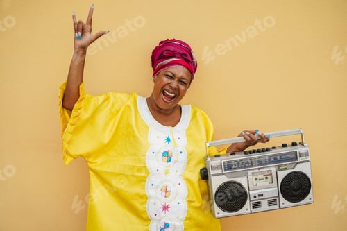 Preview: Happy senior black woman with traditional african dress dancing holding vintage stereo