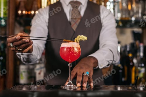 Preview: Close-up of an unrecognizable black bartender pouring a cocktail and decorating it with garnish