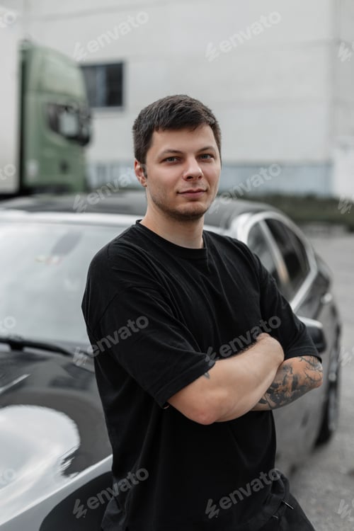 Preview: Handsome young man stands by a black car hand in hand outdoors. Rent a car, concept