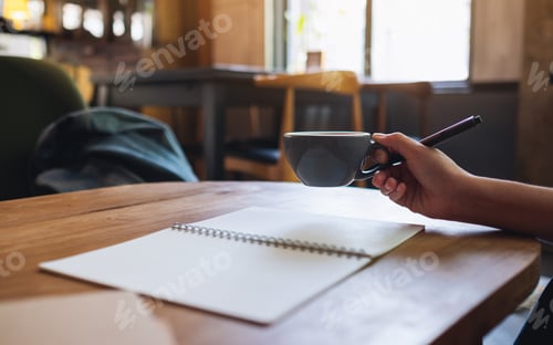Preview: Closeup image of a woman drinking coffee and writing on a blank notebook on the table