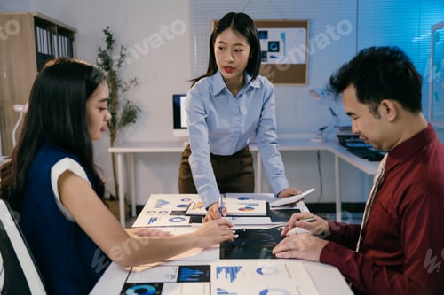 Preview: Three asian businesspeople are working late in a brightly lit modern office, collaborating on data a